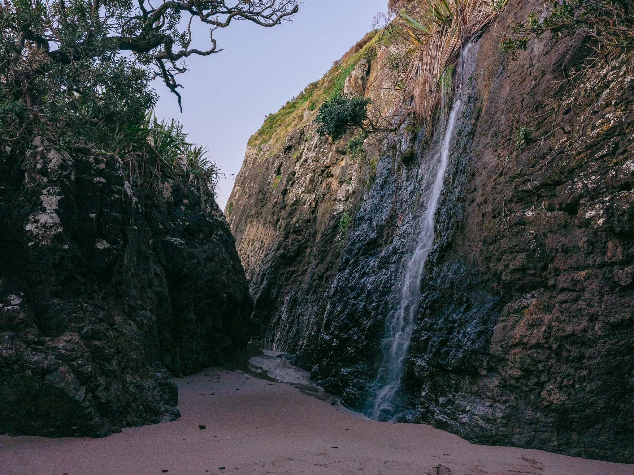 Freshwater cascade falling through a rock cleft onto a private beach