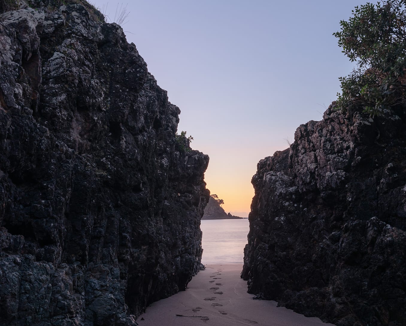 Dusk passage through ancient rock to a private beach — footprints in the sand