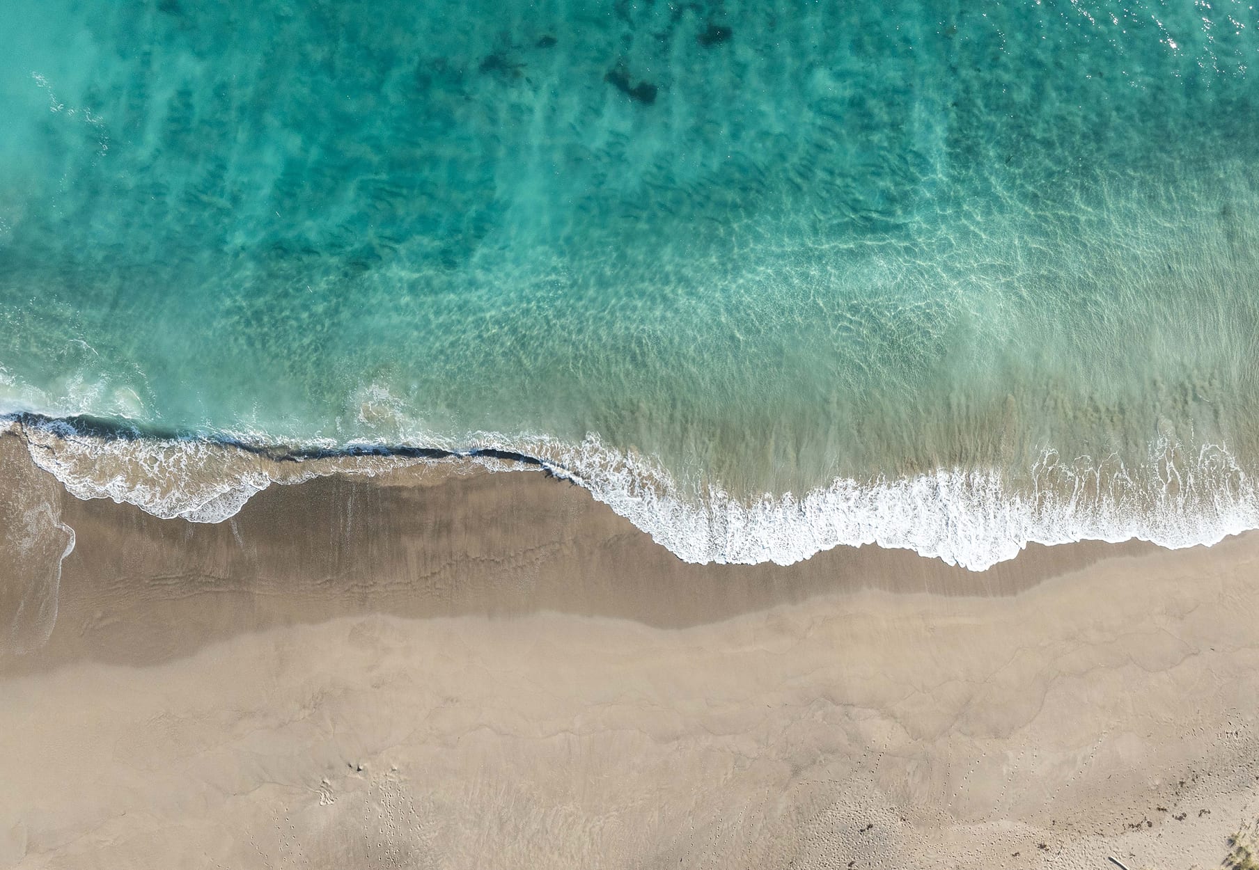 Aerial turquoise sea meeting white surf and sand at a Mataka Station beach