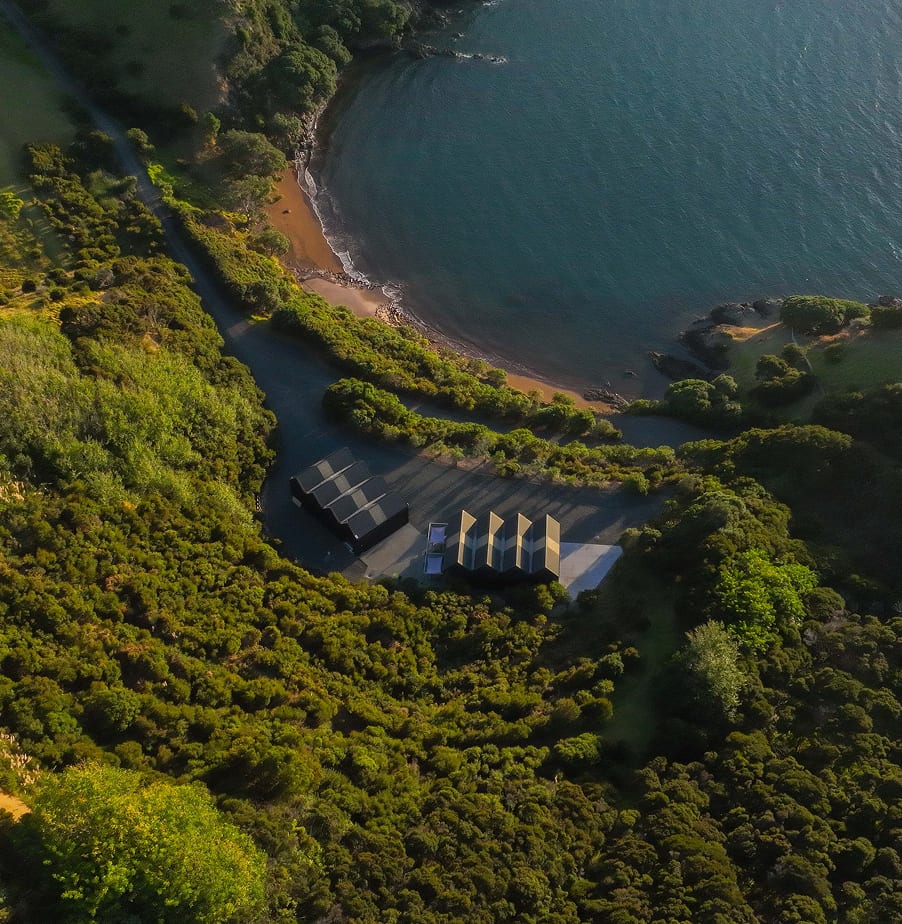 Aerial of boatsheds in native bush beside the calm waters of Whale Bay
